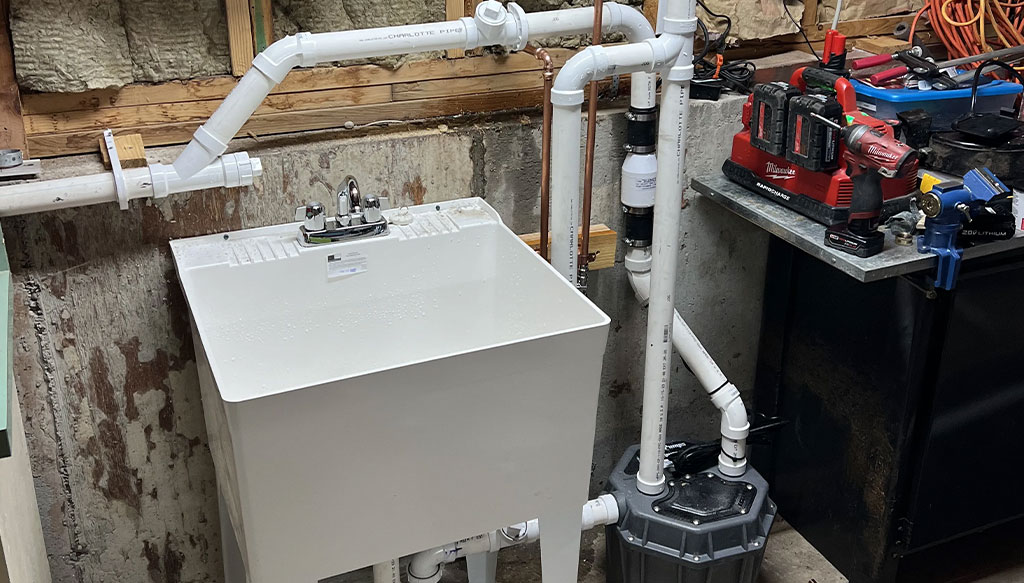 A utility sink connected to a plumbing system with PVC pipes, flanked by tools and equipment on a nearby workbench in a workshop setting.