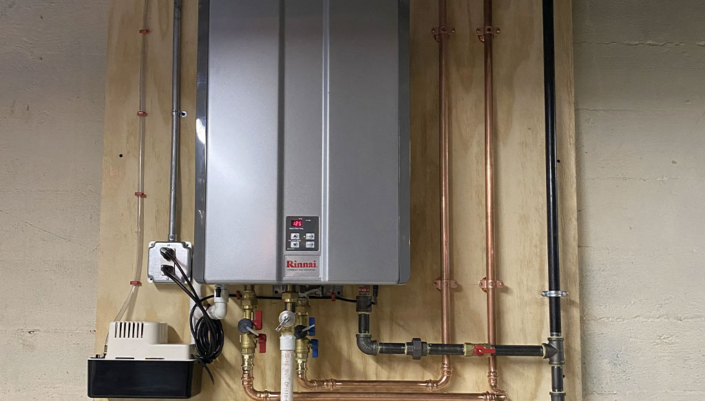 A tankless water heater mounted on a wooden board with connected pipes and electrical components.